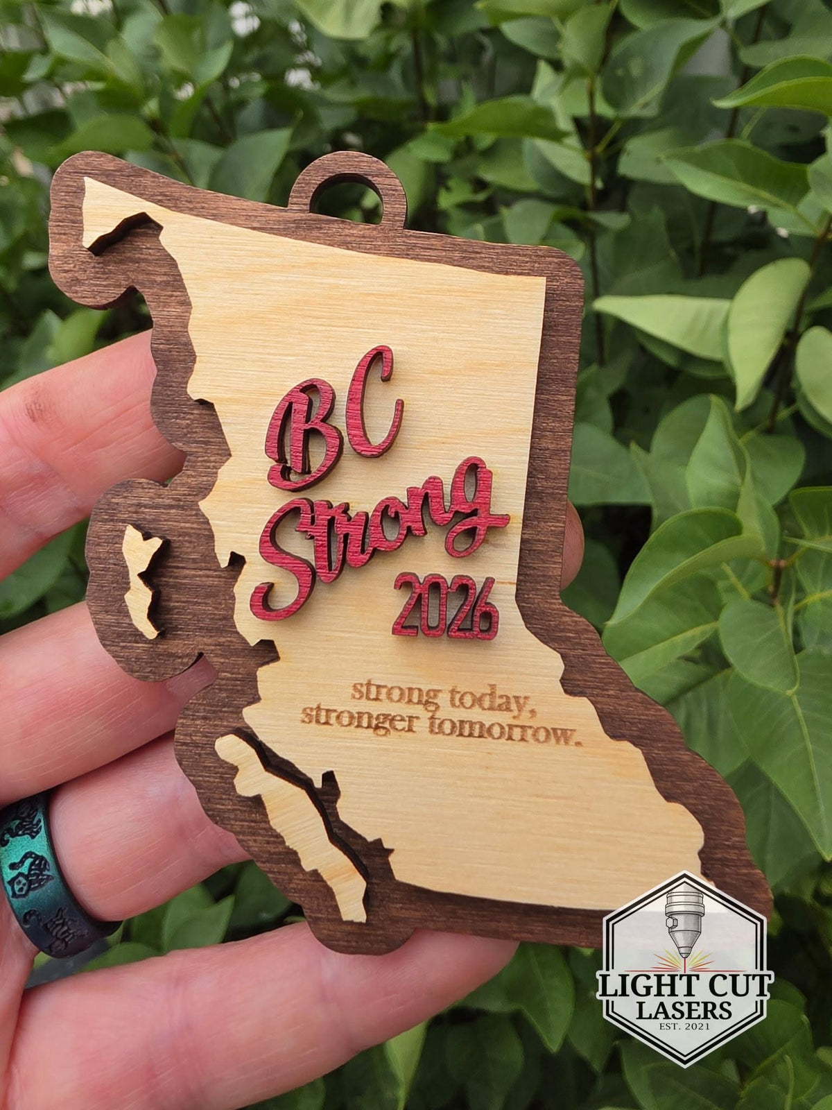 Wooden ornament in the shape of British Columbia with 'BC Strong' and '2026' in red lettering and the words 'strong today, stronger tomorrow.' lasered on the wood.