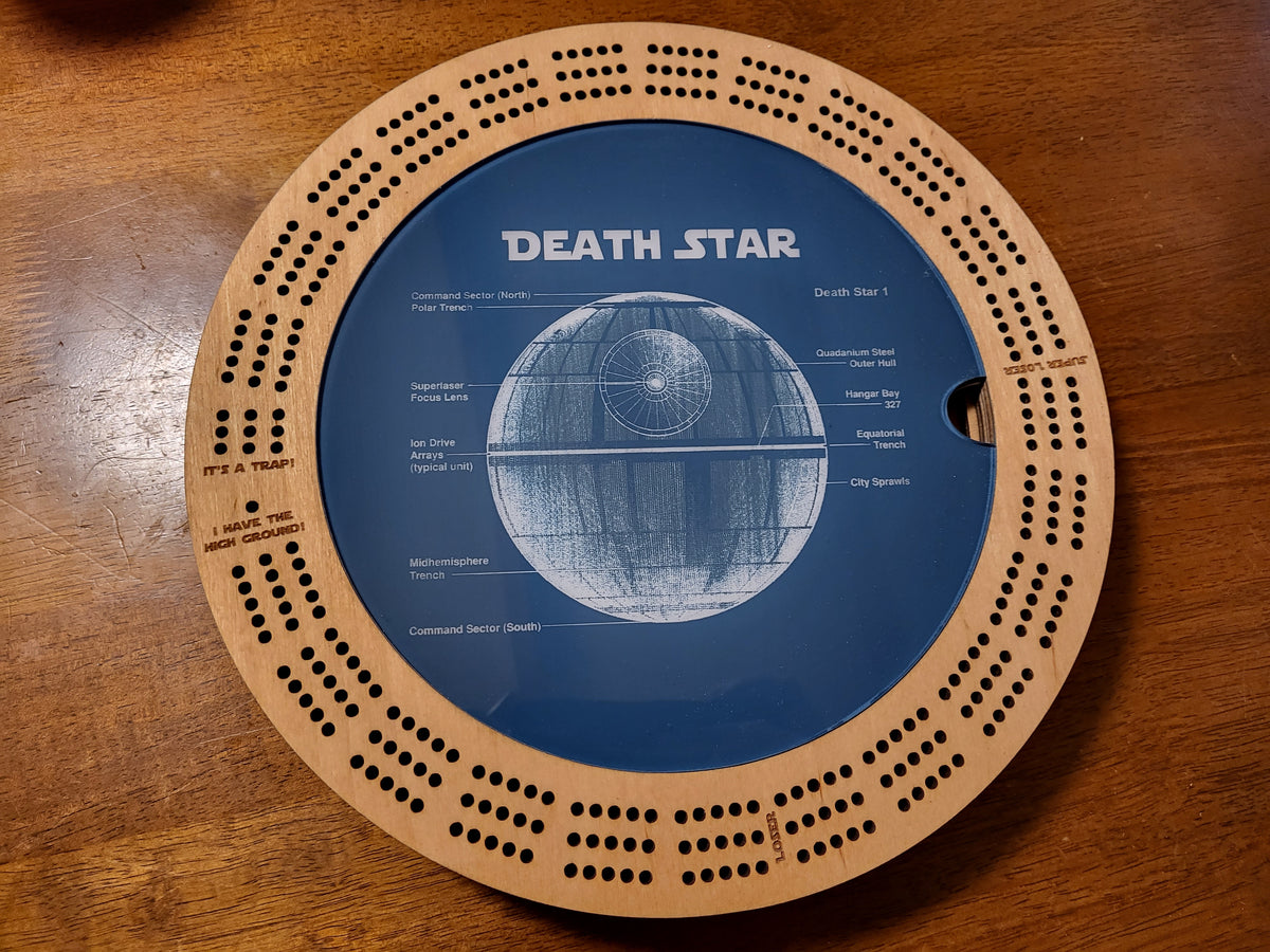 A circular wooden board game featuring a blue center with a white line drawing of the Death Star and the text 'DEATH STAR,' photographed from above on a wooden tabletop.