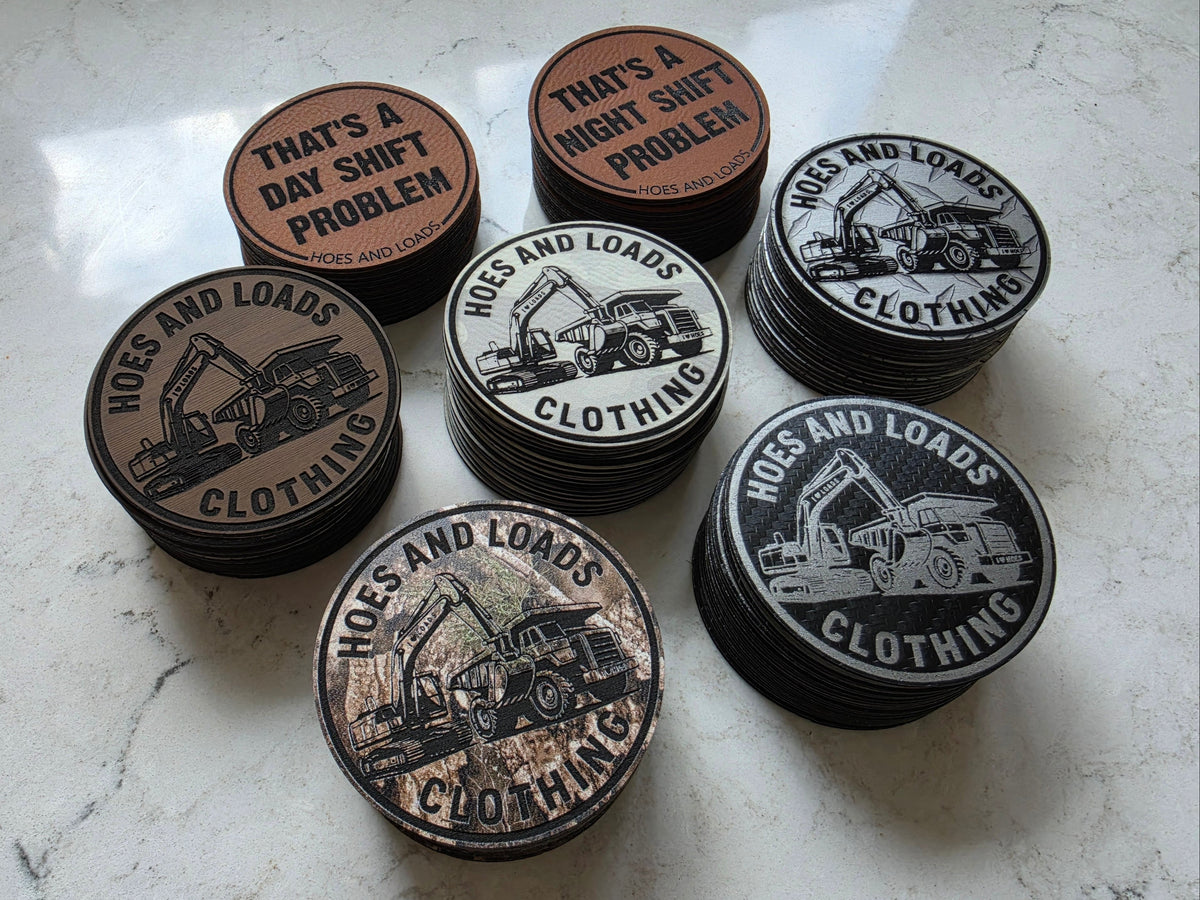 A group of round metal tins stacked together on a light marble surface. The tins feature vintage-style illustrations of excavators and the text 'HOES AND LOADING' and 'THAT'S A DAY SHIFT PROBLEM'.