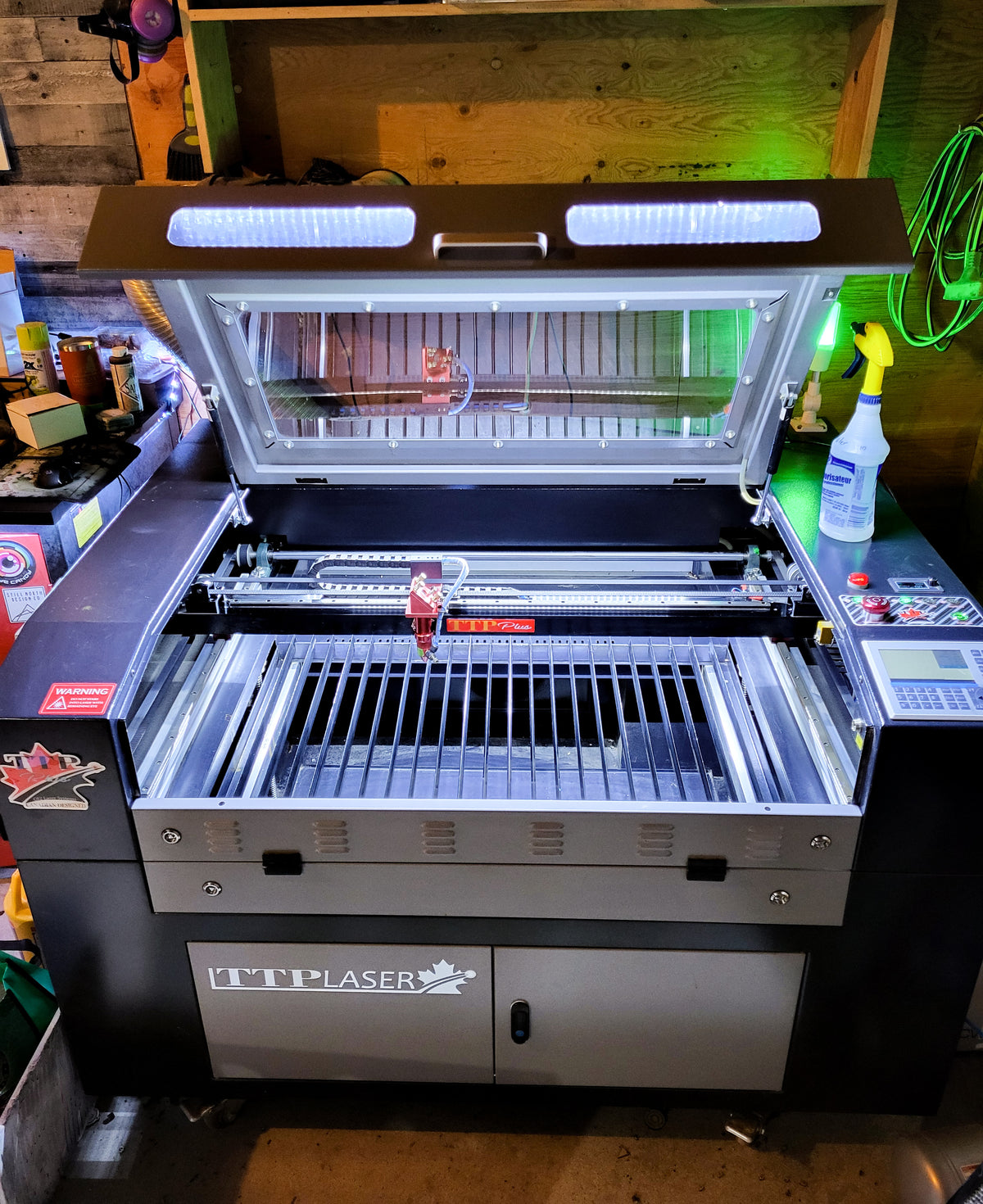 A desktop laser engraver machine with its lid open, showing the interior laser chamber and Z-axis gantry. The machine has a black and silver finish with a control panel on the right side and a brand label reading 'LTP LASER' on the front door.