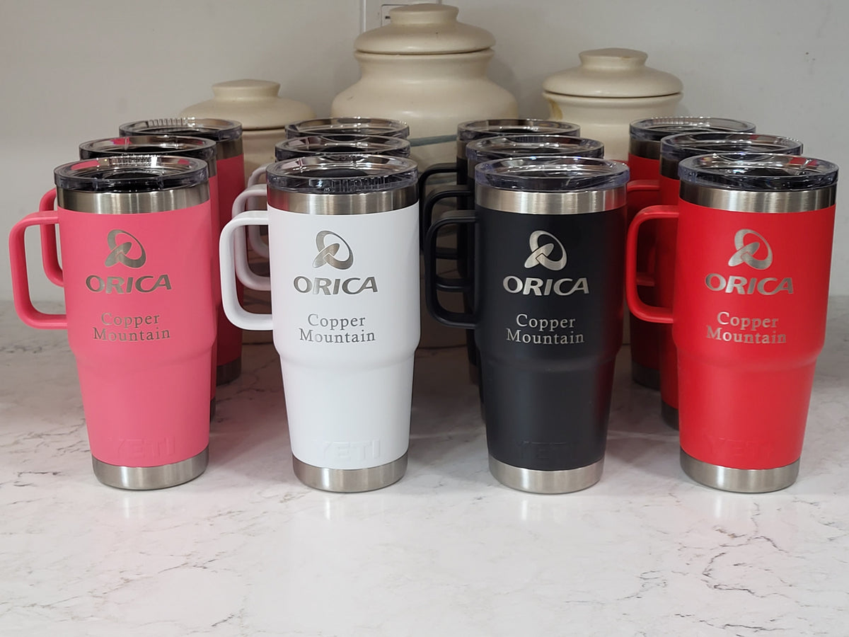 Six insulated travel mugs with handles and clear lids arranged on a light marble surface. The mugs are shown in pink, white, black, and red, with two additional mugs in the back.
