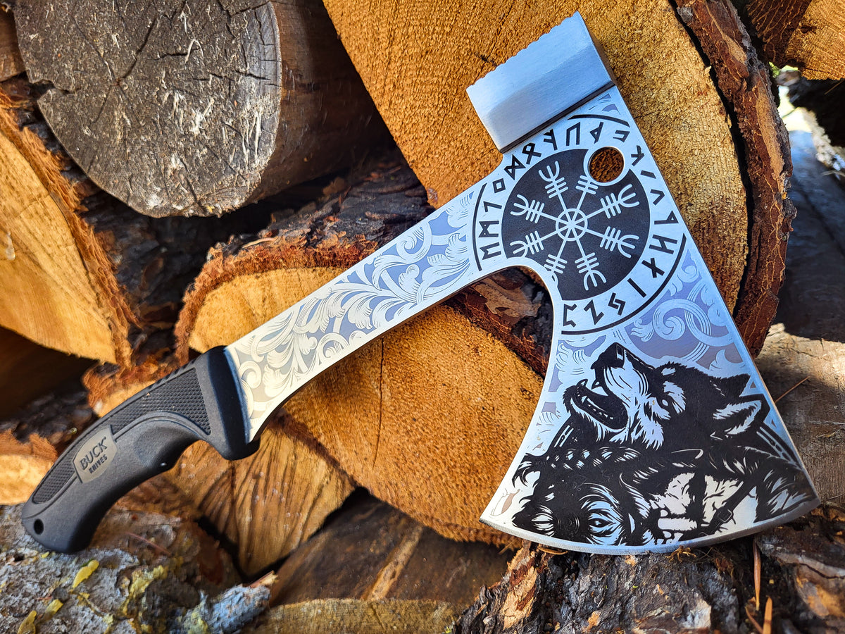 A decorative Viking-style hatchet with an engraved silver blade, black handle, and detailed wolf and rune artwork, resting on stacked firewood logs.